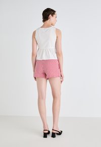 Top bianco senza maniche con vita arricciata, abbinato a pantaloni corti a scacchi rossi e bianchi. Il modello indossa sandali neri con tacco a blocco.