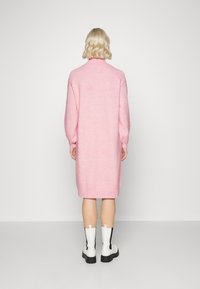 Pink knitted dress with a high neckline, long sleeves, and ribbed cuffs; paired with white ankle boots featuring a black accent.