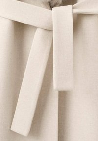 Tela de lana beige con textura suave que presenta un detalle destacado de un lazo atado en el cuello, realzando el diseño de la prenda.