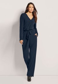 Navy blauwe jumpsuit met lange mouwen, V-hals, tailleband en zijzakken; gemaakt van zachte, gestructureerde stof.
