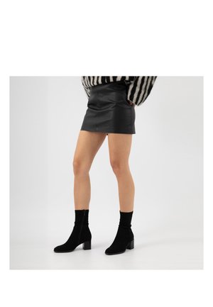 Osoba nosząca czarne zamszowe botki na słupku, krótką czarną skórzaną spódnicę oraz czarno-biały sweter w paski.