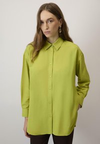 Camicia verde lime con bottoni, colletto, maniche lunghe e vestibilità rilassata. Realizzata in tessuto morbido, con tasche laterali e orlo curvo.