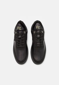 Svarta sneakers med en kombination av slät läder och mocka, en perforerad tådesign, svarta skosnören och en liten grön logotyp på tungan.