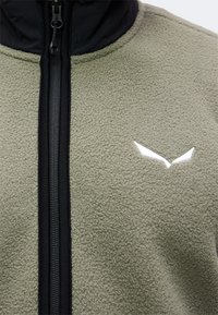 Κοντινό πλάνο ενός γκρι fleece μπουφάν με μαύρο φερμουάρ και μικρό λευκό λογότυπο σε σχήμα πουλιού στο στήθος.