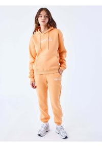 Perzikenkleurige hoodie met een voorzak en trekkoorden, gecombineerd met bijpassende joggers met een geborduurd logo. Textuurstof; comfortabele pasvorm.