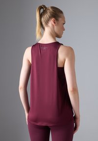 Burgundi värvi sportlik tank top, mis on mugava lõikega, ilma varrukateta ja pehmest kangast; selja kaeluses on logo ja pind on sile.
