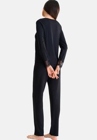 Ensemble noir à manches longues et pantalon en tissu doux, avec des accents de dentelle à pois transparents sur les poignets. Design minimaliste, forme ajustée.