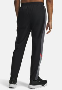 Black athletic pants featuring a tapered design, elastic waistband, contrasting gray side panels, and red accents.