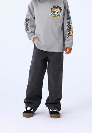 Dziecko ubranie w szarą bluzę z długim rękawem z nadrukiem kreskówkowego hamburgera i napisem, luźne czarne spodnie oraz czarne trampki z białymi sznurowadłami i gumowymi podeszwami.