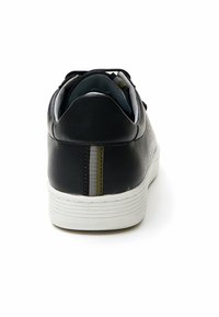 Black leather sneaker with a textured finish, white rubber sole, and grey lining. Features a vertical striped accent detail on the heel.