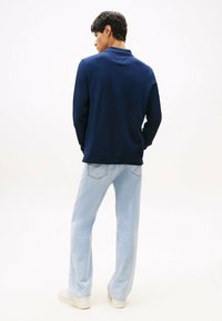 Polo de manga larga de color navy con un acabado texturizado, combinado con jeans de pierna ancha de color azul claro y zapatillas blancas. Detalle visible en el cuello trasero.