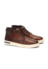 Bruine leren enkelschoenen met suède accenten en witte rubberen zolen. Voorzien van zwarte veters en branding op de tong en zijkant.