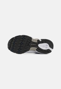 Semelle de chaussure de sport noir, gris et blanc dotée d'un motif texturé avec des crampons pour l'adhérence et un logo de marque visible sur le midsole.