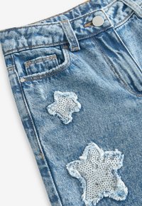 Pantalones cortos de mezclilla en azul claro con bordes deshilachados. Presenta dos parches en forma de estrella con lentejuelas plateadas, cierre de botón y un bolsillo delantero.