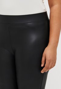 Fekete leggings sima, fényes anyagból, széles derékpánttal. Simább kialakítást és szoros illeszkedést mutat, kiemelve a test vonalait.