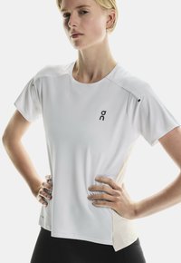 T-shirt de sport blanc à manches courtes, avec un col rond, un tissu texturé et un petit logo noir sur le côté gauche à l'avant.