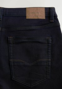 Tmavé džíny z denimu s zadní kapsou zdobenou kontrastním šitím a hnědým koženým štítkem na pásku.