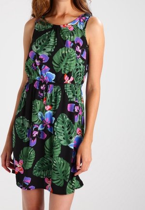Vestido negro sin mangas con hojas tropicales verdes y flores moradas, azules y rosas, llevado por una mujer mostrada desde los hombros hasta la mitad del muslo.