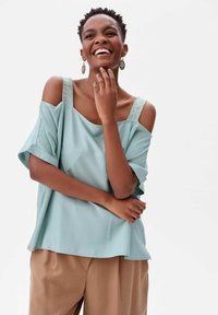 Jasnoniebieska bluzka bez ramiączek z krótkimi rękawami i dekoracyjnymi paskami. Miękka tkanina, luźny krój, połączona z beżowymi spodniami.