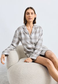Ljus rutigt sovset i beige, grått och vitt som består av en knapp-up skjorta med krage och lång ärm, i kombination med shorts.