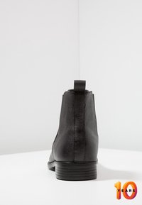 Černá kožená kotníková bota s texturovaným povrchem, kulatou špičkou a podpatkem. Obsahuje poutko pro snadné obouvání. Minimalistický design, žádné viditelné akcenty.