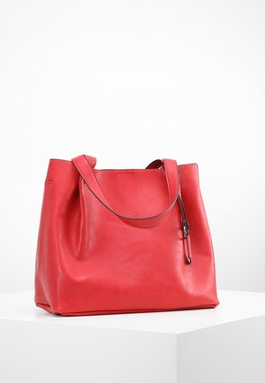 Czerwona skórzana torba typu tote z pojedynczym paskiem na ramię i małą klamrą, umieszczona na białej powierzchni na jednolitym białym tle.