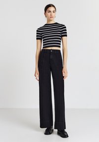 Jeans a vita alta neri a gamba larga abbinati a una maglietta cropped a righe bianche e nere. L'outfit presenta maniche aderenti e un design essenziale.
