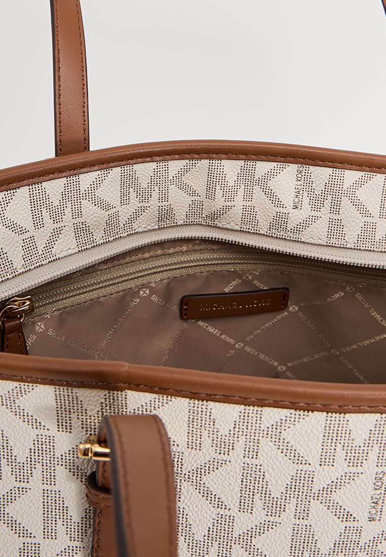 Sac à main beige avec des accents marron, comportant une poche zippée à l'intérieur et une doublure à motifs avec le nom de la marque, fabriqué en cuir texturé.