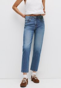 Ljusblå denimjeans med rak passform, blekt mönster, femfickdesign och sömnadsdetaljer. Bärs med bruna mockaskor.