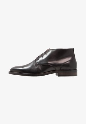 Schwarzer Leder-Herren-Derby-Schuh mit Schnürsenkeln, leicht spitz zulaufender Zehenpartie und niedrigem gestapeltem Absatz auf weißem Hintergrund.