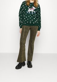 Sudadera verde con lunares blancos y un gráfico de un perro; combinada con pantalones de campana dorados brillantes y zapatillas negras de suela gruesa.