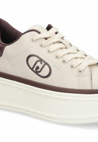 Sneaker in pelle beige con accenti marrone scuro, design con lacci, linguetta testurizzata e suola in gomma sollevata. Logo sul lato.