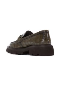 Mocasines de color verde oscuro con textura de cocodrilo, con una amplia punta redondeada, una correa decorativa y una suela gruesa con tacos de color marrón.