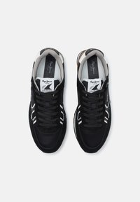 Μαύρο αθλητικό παπούτσι με άνω μέρος από σουέτ και πλέγμα, επενδεδυμένος γιακάς και αντίθετες λευκές λεπτομέρειες. Διαθέτει κορδόνια και λογότυπο στην γλώσσα.