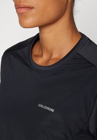 Zwarte sportshirt met een ronde hals, korte mouwen en een gladde textuur. Bevat een zilveren 'Salomon' logo op de voorkant.