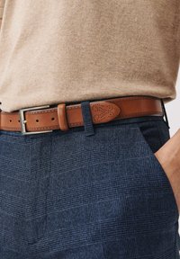 Pantalons à carreaux navy en tissu texturé, accompagnés d'une ceinture en cuir marron avec des perforations décoratives et une boucle en métal argenté.