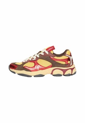 Zapatilla deportiva con malla amarilla, ante marrón y detalles metálicos rojos, suela beige, cordones blancos y lengüeta con marca.