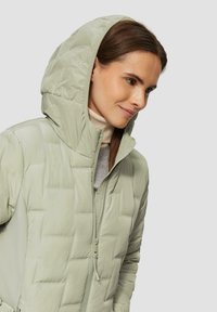 Hellgrüne, gesteppte Pufferjacke mit Kapuze, ausgestattet mit einem Reißverschluss und strukturierten Einsätzen. Glatter, weicher Stoff mit strukturiertem Design.
