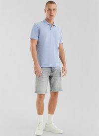 Polo shirt bleu clair à manches courtes, assorti avec un short en denim gris. Des baskets blanches et des chaussettes blanches côtelées complètent le look décontracté.