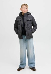 Svart puffjacka med huva, två bröstfickor och dragkedjestängning, kombinerad med ljusblå vida jeans och mörka skor.