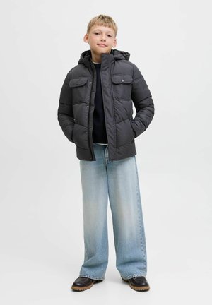 Veste matelassée noire avec une capuche, deux poches poitrine et une fermeture éclair, associée à un jean large bleu clair et des chaussures foncées.