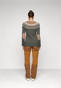 Gebreide trui in donkergroen met witte en bruine gebreide yoke, elleboogpatches, gecombineerd met bruine broek. Glad, gestructureerd stof.