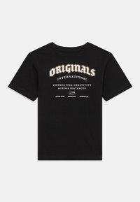 Juodos trumpomis rankovėmis marškinėliai su tekstu "ORIGINALS INTERNATIONAL Connecting Creativity Across Distances" spausdintu baltais ir smėlio spalvos rašmenimis ant nugaros.