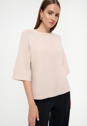 Suéter de punto rosa claro con mangas 3/4, cuello redondo y textura suave, combinado con pantalones negros. Diseño sencillo, sin estampados.