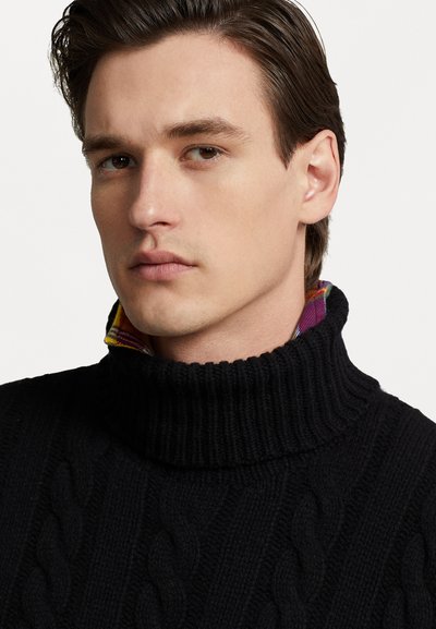 Melnā adīta turtleneck džemperis ar ribotu apkakli, kurā no apkakles iznāk krāsains kareklis.