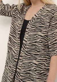 Kevyt beige kimono mustilla seepra raidalla, jossa on kolme neljänneshihoja ja avoin etuosa. Huomaamaton tekstuuri näkyvissä.