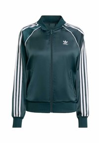 Mörkgrön satin bomberjacka med vita ränder längs ärmarna, ribbade muddar och fåll, samt dragkedja framtill. Har en logotyp på bröstet.