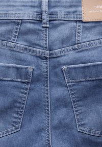 Ljusblå denimjeans med en slät yta, fem fickor och kontrasterande sömmar. Taggen som är sydd på midjebandet visar varumärket.