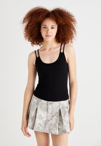 Top negro sin mangas con tirantes finos y un diseño ajustado, combinado con una falda plisada gris claro con un patrón de hojas.