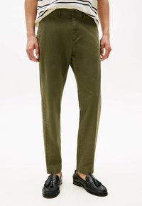 Pantaloni verde oliva con taglio dritto, realizzati in tessuto leggero, con tasche frontali e una texture liscia, abbinati a mocassini neri.